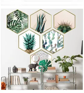 Detail of hexagonal golden frames featuring green tropical plant prints on a white wall