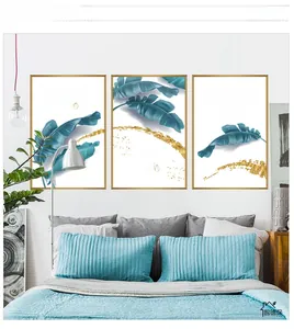 Three-piece set of tropical banana leaf wall art in gold frames above a blue bed