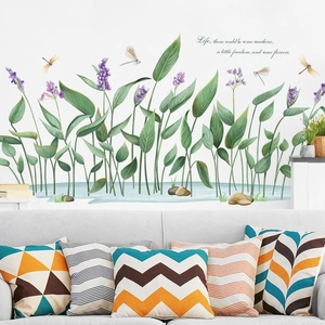 Watercolor wall sticker with green leaves, dragonflies and stones behind a modern sofa