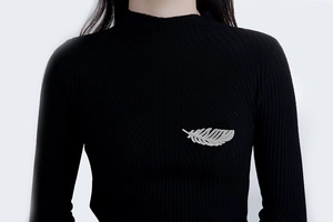 Detail of silver feather brooch with zircon inlay pinned on a black sweater