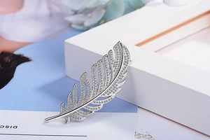 Macro shot of silver feather brooch with sparkling zircons on elegant blue background