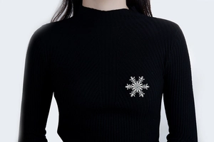 Détail de la luxueuse broche flocon de neige argentée avec zircons sur un pull noir