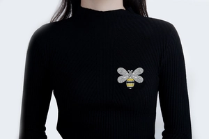 Detailed view of a silver bee brooch with zircons pinned to a black turtleneck sweater