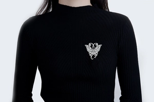 Détail de broche papillon argentée avec zircons sur un pull noir à col roulé