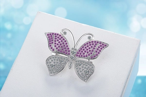 Macro shot of silver butterfly brooch with pink and white zircon stones on white stand