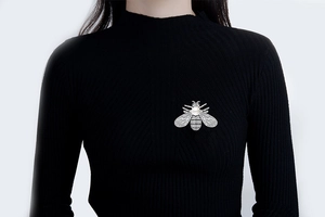 Detailed close-up of a bee-shaped brooch with white pearl and rhinestones on black fabric