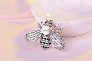 Macro shot of bee brooch with large pearl, crystal wings, and rose gold details