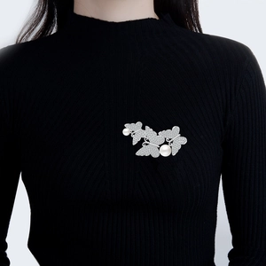 Elegante spilla a farfalla argentata con perle e cristalli su un maglione nero a costine