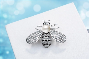 Macro shot of bee brooch featuring pavé zircon, silver metal plating, and a round white pearl