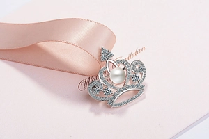 Close-up of crown brooch with white pearl and zircons on wedding invitation gift card