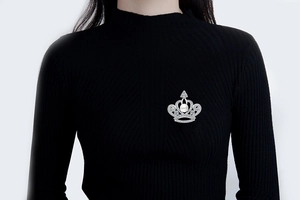 Detail view of a luxury silver crown brooch with white zircons and a pearl on black fabric