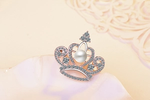 Macro shot of rose gold crown brooch with sparkling zircons and a white pearl accent