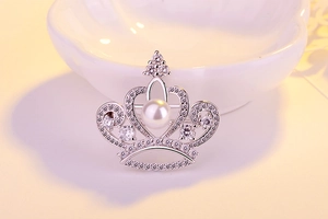 Detailed macro of silver crown brooch featuring a white pearl and sparkling crystals