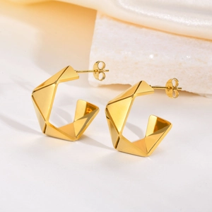 Detalle macro de pendientes geométricos bañados en oro con textura facetada sobre seda