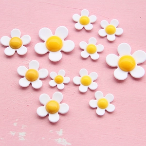 Flat lay of small acrylic daisy charms in various sizes for DIY phone case crafts