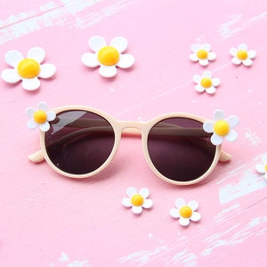 Beige round frame kids sunglasses with 3D daisy flowers on a pink wood background