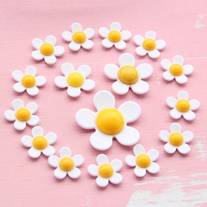 Flat lay of multiple sizes of white daisy acrylic flower charms on pink wood background