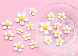 Flat lay of small white acrylic daisy charms in two sizes for DIY craft decorations