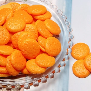 Macro detail of orange resin cookie charms for DIY crafts on a white marble surface