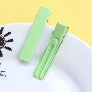 Close-up of mint green macaron hair clips on a white ceramic plate with a yellow background