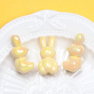 Macro view of three yellow iridescent bunny beads in a white porcelain dish for DIY