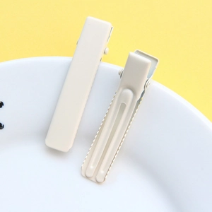 Close-up of two cream-colored metal alligator hair clips on a decorative plate
