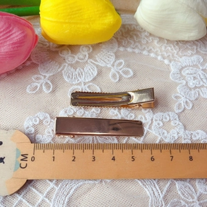 Macro detail of 4.8cm gold plated metal duckbill hair clips on white lace fabric
