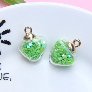 Detailed view of a heart-shaped glass pendant filled with green star sequins and gold clasp