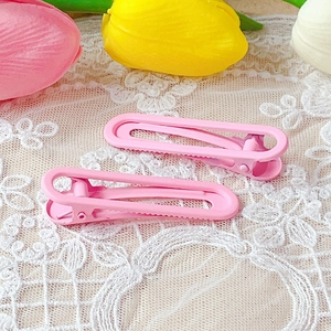 Close-up of pink matte metal duckbill hair clips on white lace fabric with tulips