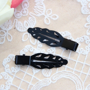 Macro shot of black leaf-shaped hair clips with hollow veins on white lace background