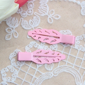 Macro detail of leaf-shaped pink hair clips with hollow design on white lace background