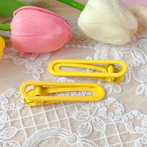 Close-up of bright yellow matte duckbill hair clips on white floral lace fabric