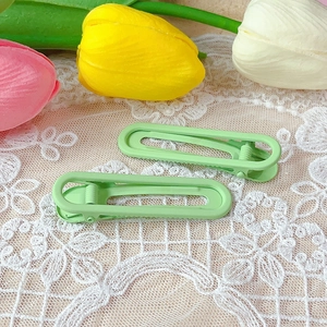 Close-up of matte light green hollow hair clips on a white lace background with tulips