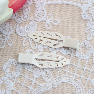 Close-up of cream leaf-shaped metal hair clips with hollow design on lace background