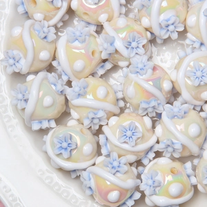 Macro detail of creamy acrylic beads with blue floral relief and rainbow luster finish