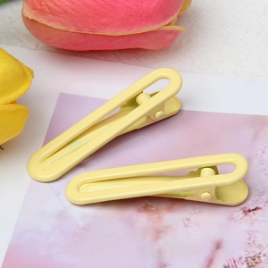 Close-up of two bright yellow metal hair clips on a soft pink background with tulips