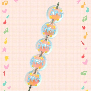 Detailed macro view of five acrylic Christmas beads with orange core and Bells text pattern