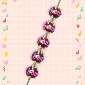 Detailed close-up of acrylic DIY beads with holly script and pink grid background