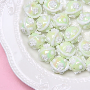 Close-up of mint green pearlescent beads with 3D white floral details for DIY jewelry