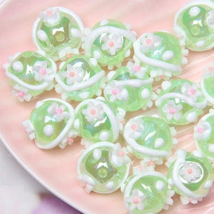 Macro shot of light green resin DIY beads with floral decor on a pink tray