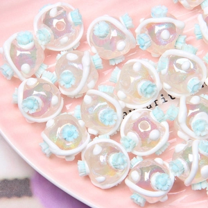 Macro view of iridescent DIY aurora beads with blue flowers in a pink ceramic tray