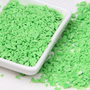 Detailed close-up of bright green polymer clay crumbs for DIY crafts in a white tray