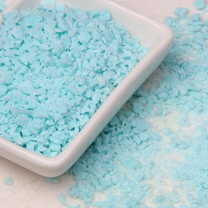 Detailed view of light blue irregular sprinkles on a white ceramic dish for DIY craft projects