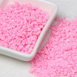 Close-up of pink irregular polymer clay crumbs scattered on a white tray and fabric
