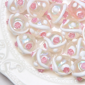 Macro shot of iridescent round beads with pink rose details and white relief for DIY jewelry