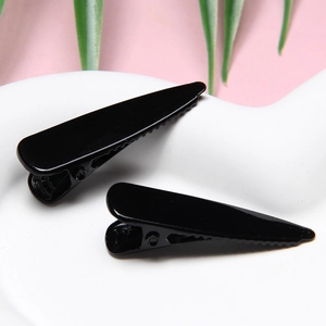 Close-up of black non-slip hair clips with glossy finish on a minimalist ceramic base