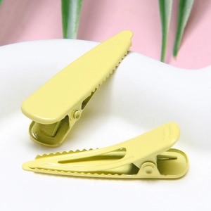 Detail of yellow macaron metal hair clips on a ceramic stand with a pink background