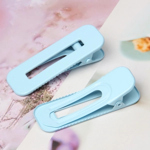 Macro shot of two light blue rectangular cutout hair clips with a matte finish and sawtooth grip