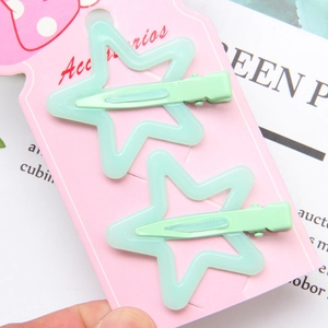 Detail of two mint green star-shaped hair clips on a pink dotted display card