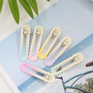 Gros plan de six barrettes à cheveux dégradées macaron sur fond de feuilles tropicales